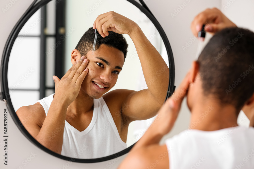 Young African-American guy using serum for skin care in bathroom