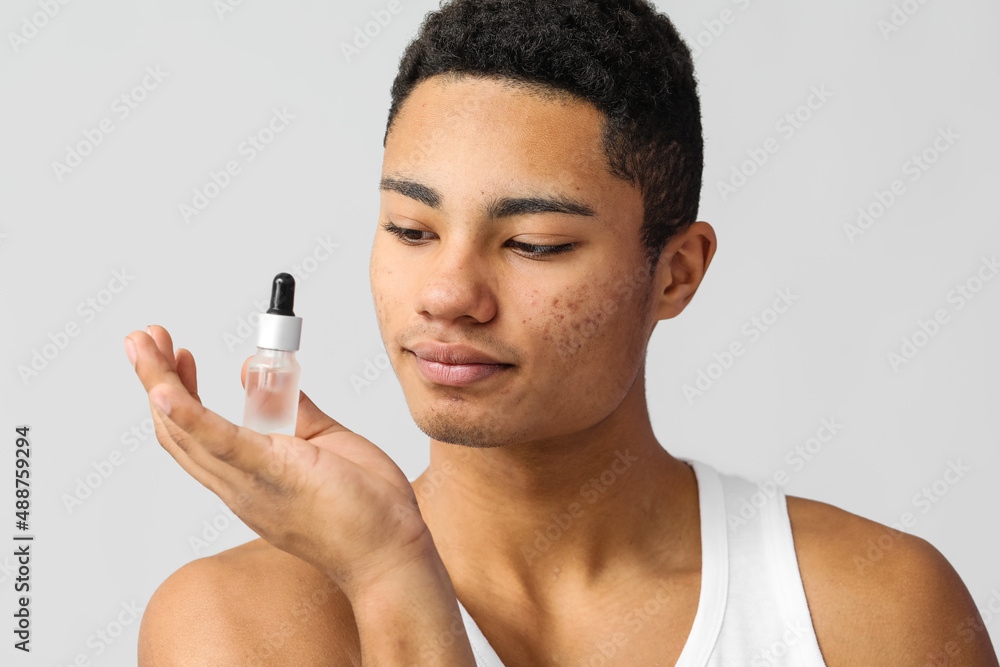 Young African-American guy with serum for skin care on grey background