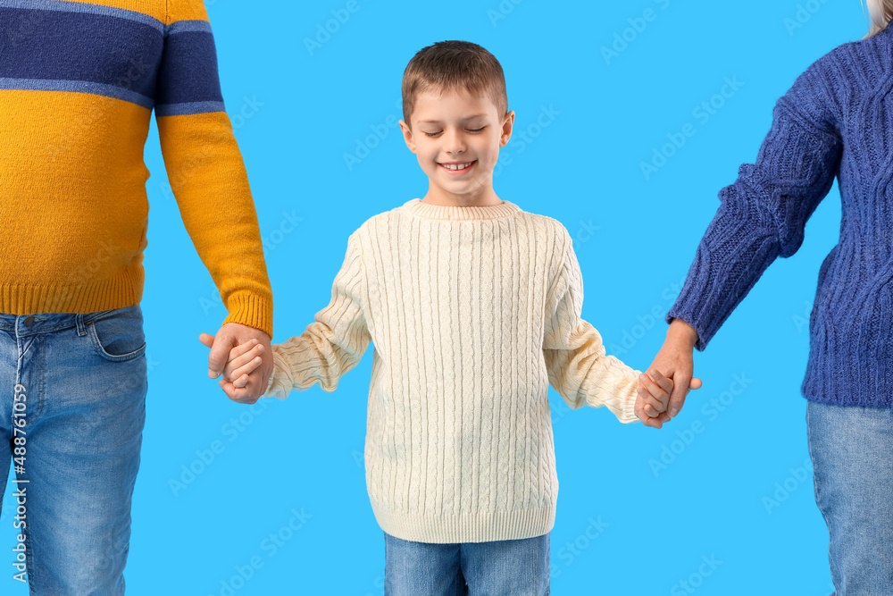 Little boy with his grandparents in warm sweaters holding hands on blue background