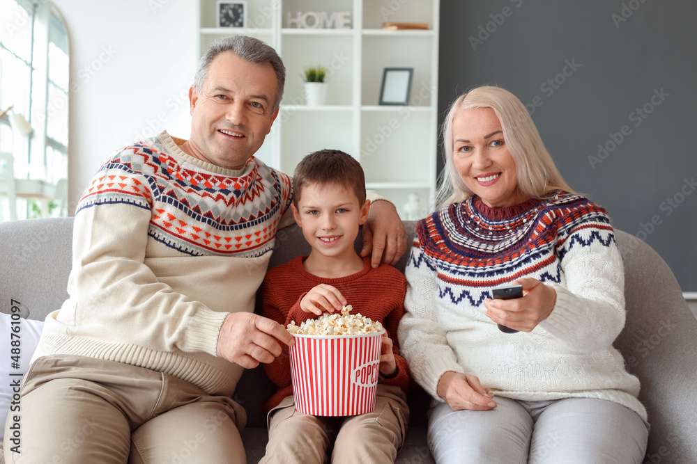 Little boy and his grandparents in warm sweaters with popcorn watching TV at home