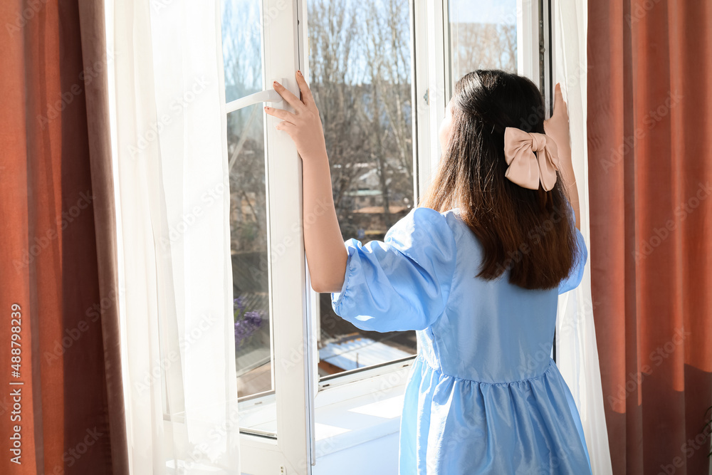 Pretty young Asian woman opening window in room