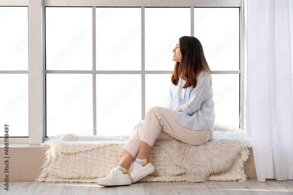 Pretty young Asian woman sitting on window sill