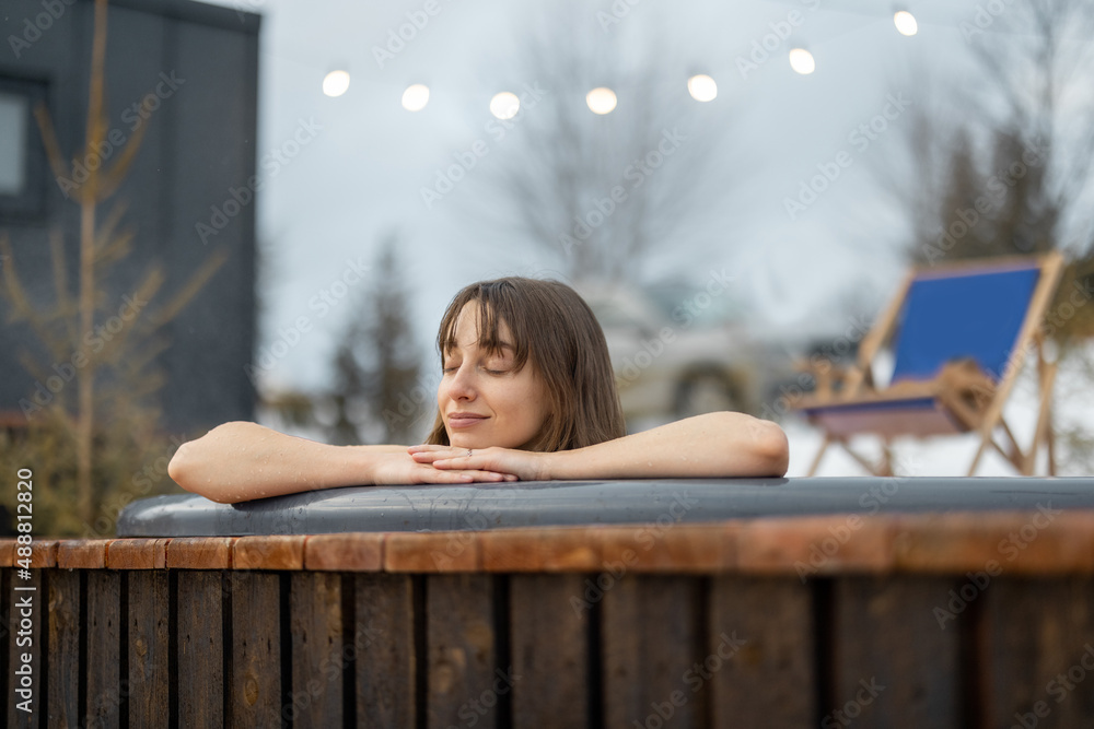 Young woman bathing in hot tub at mountains during winter. Concept of rest and recovery in hot vat. 