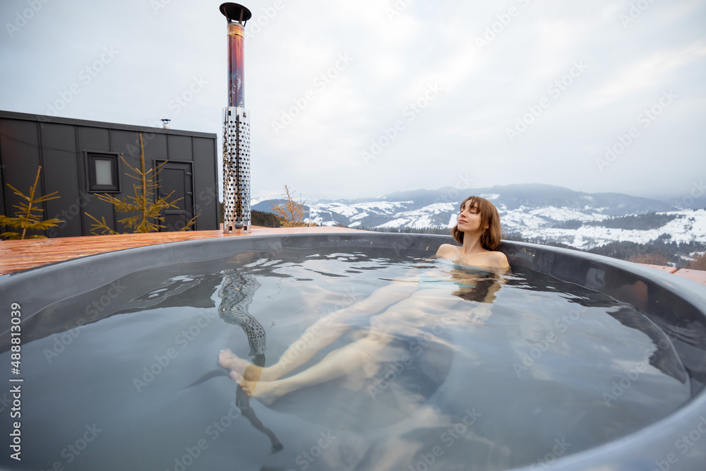 Woman swims in hot bath while resting at small modern house in the mountains on winter. Concept of r