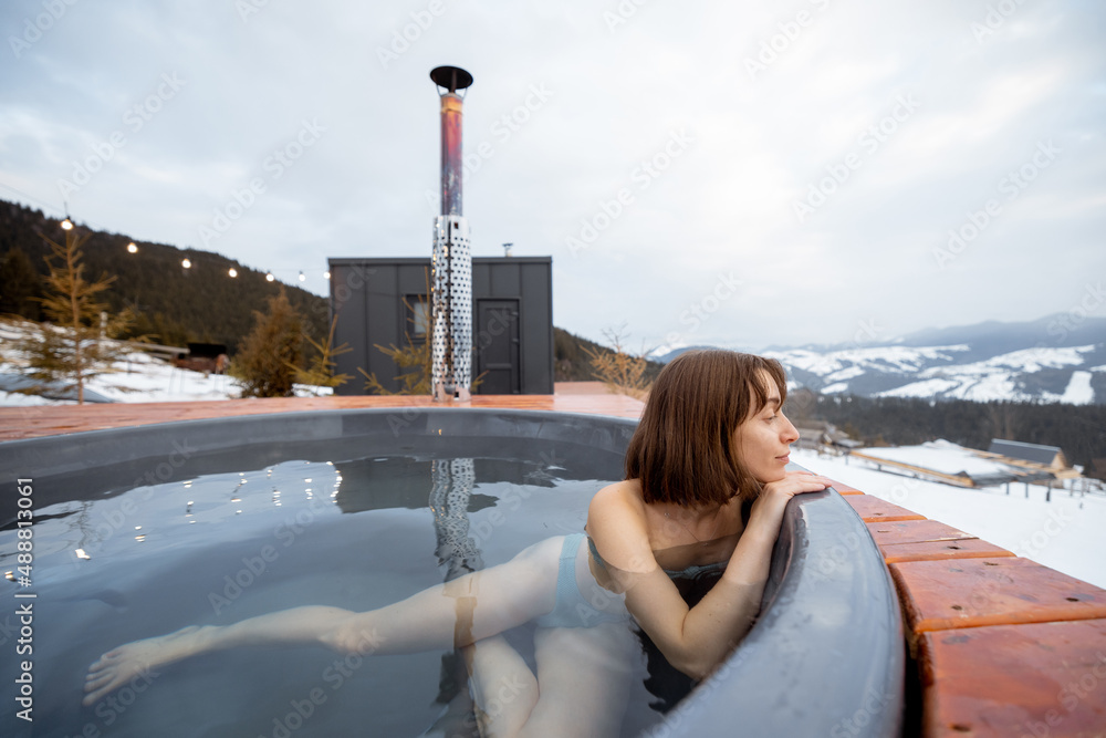 Woman swims in hot bath while resting at small modern house in the mountains on winter. Concept of r