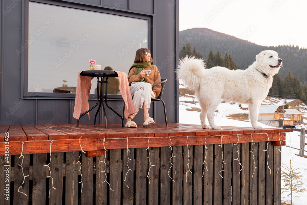 Woman with her dog resting on terrace of tiny house in the mountains on winter time. Concept of smal