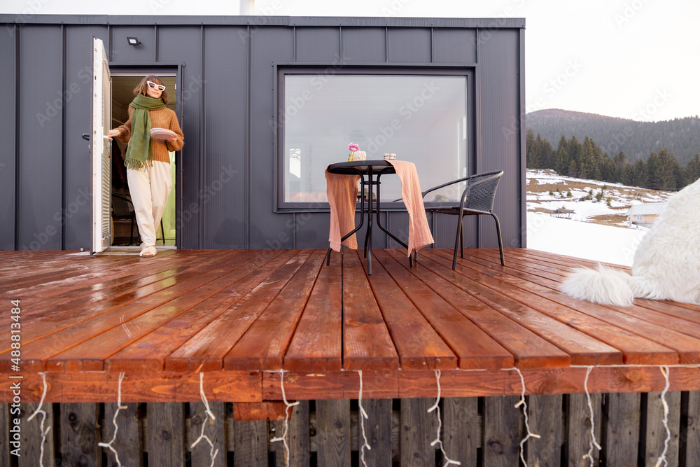 Woman going out on terrace of tiny house in the mountains. Concept of small modern cabins for rest a