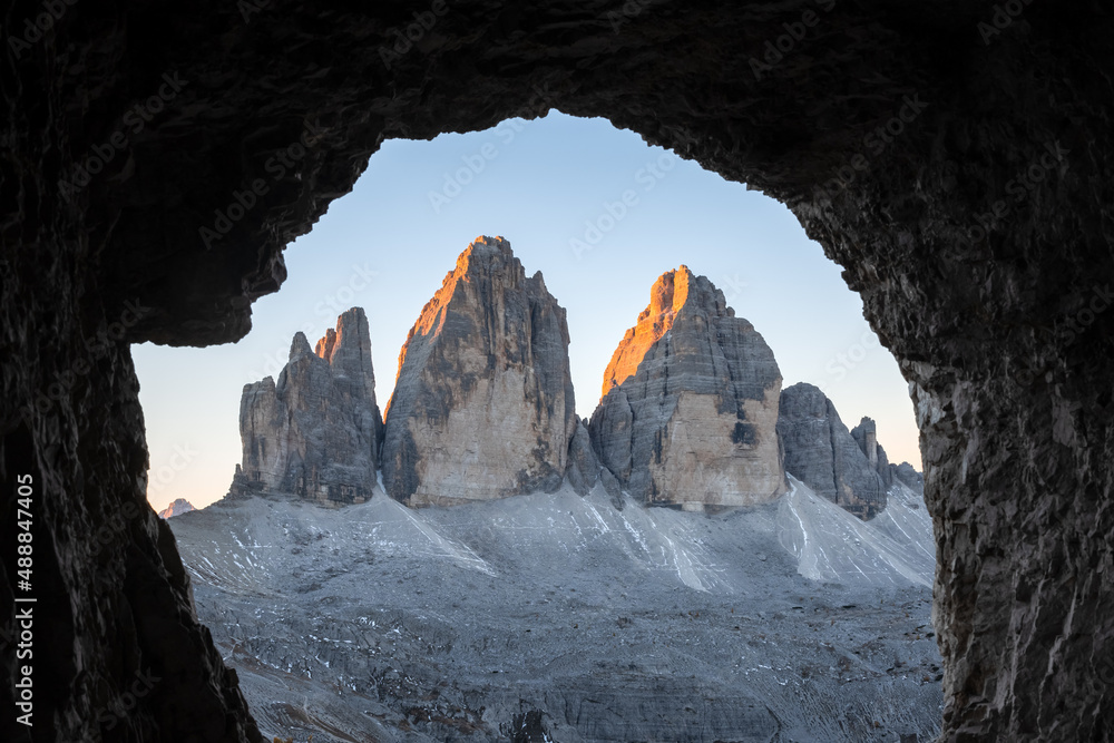 Tre Cime Di Lavaredo peaks in incredible orange sunset light. View from the cave in mountain against