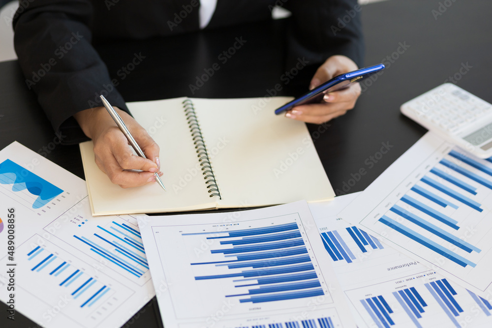 Woman writing on notepad and business analysis using mobile.