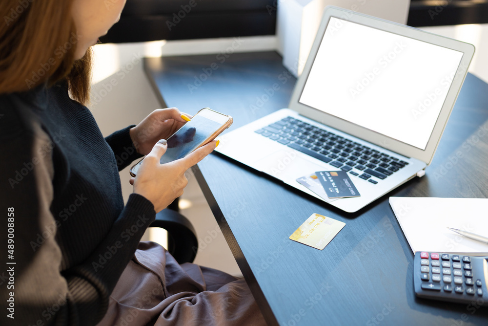 Woman using mobile phone and credit card on desk with laptop with blank screen for copy space. Onlin