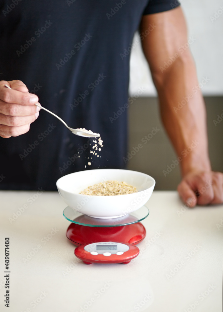 分量是关键。一个肌肉发达的男人在秤上测量早餐燕麦的裁剪图。