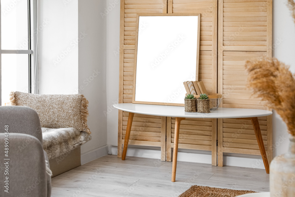 Coffee table with frame, books and flowerpots near wooden folding screen in living room