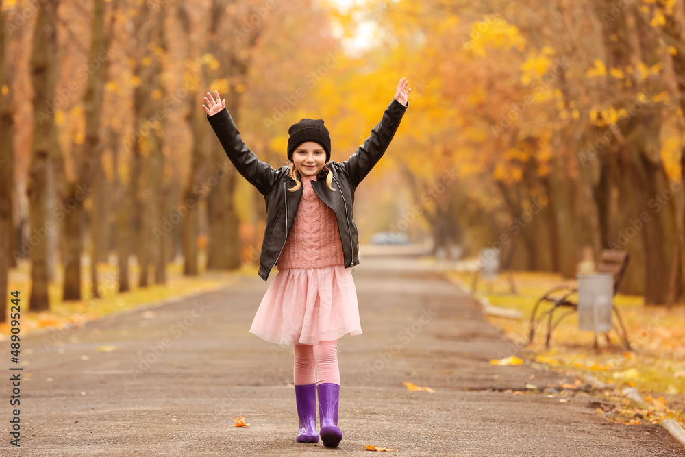 Little girl in stylish rubber boots walking in autumn park