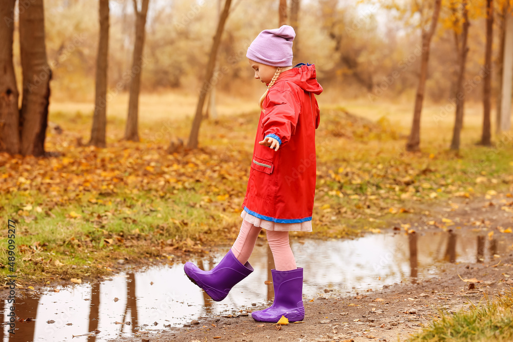 Little girl in rubber boots near puddle in autumn park