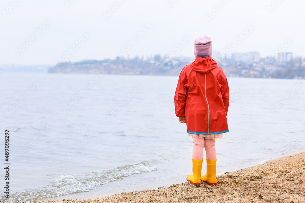 穿着时髦橡胶靴和雨衣的小女孩在河边散步