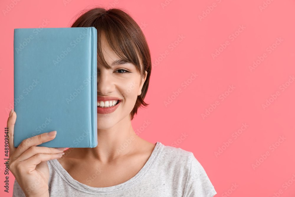 Beautiful young woman with book on pink background