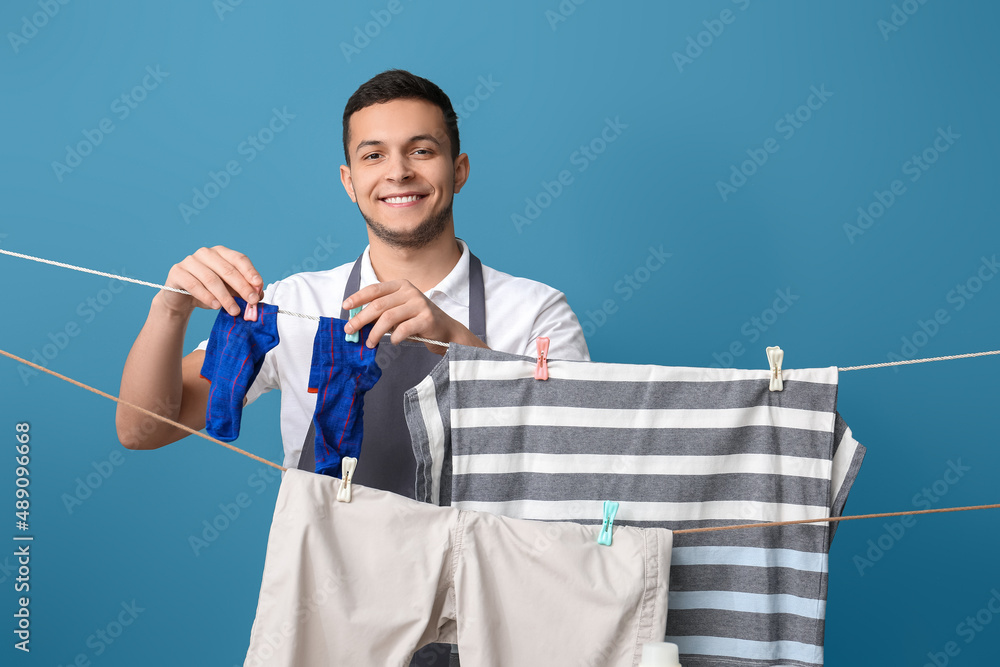 Young man hanging clean socks with clothespins on blue background