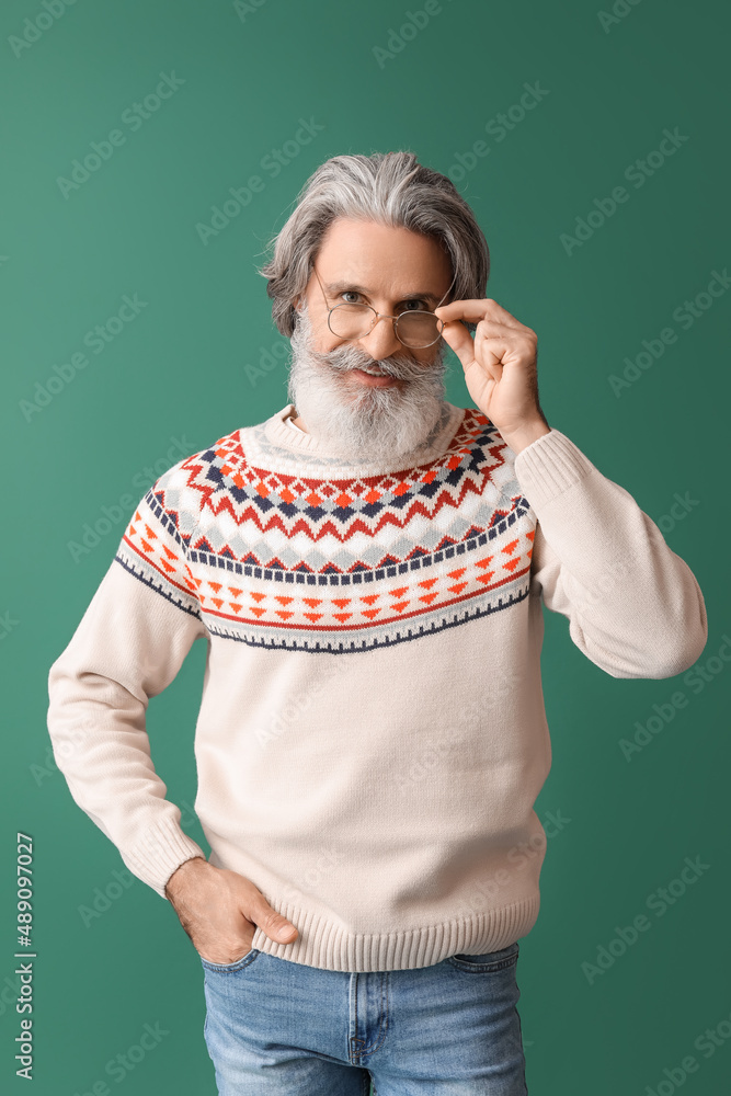 Handsome senior man in knitted sweater on green background