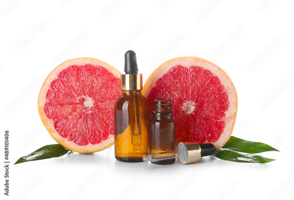 Bottles of essential oil and ripe grapefruit on white background