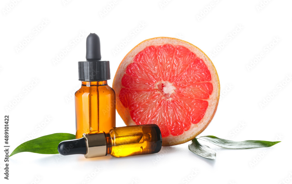 Bottles with essential oil and half of grapefruit on white background