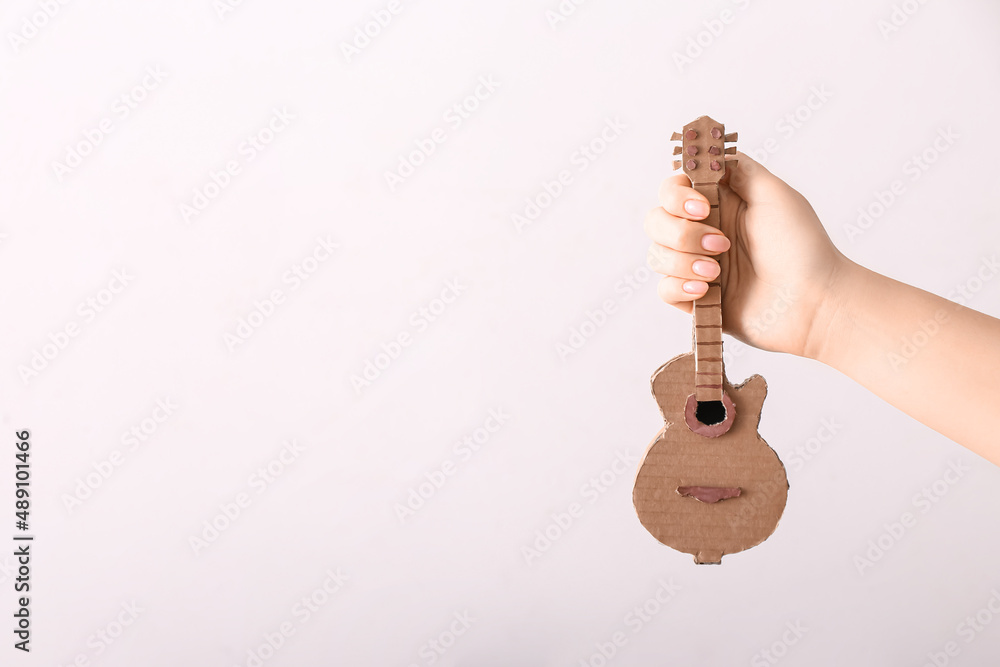 Female hand with cardboard guitar on light background