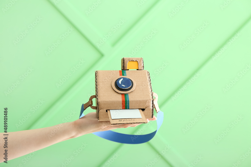 Female hand with cardboard photo camera on color background