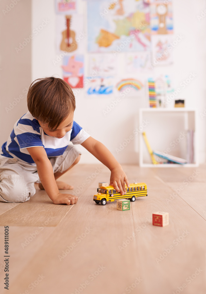 The wheels on the bus go round and round. Shot of a cute little boy playing with his toys in his roo