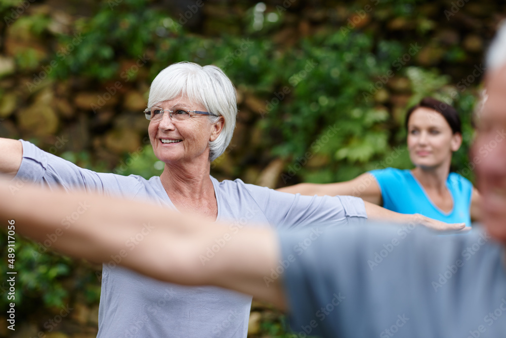 Keep calm and do yoga. Shot of a senior woman doing yoga with other people outdoors.