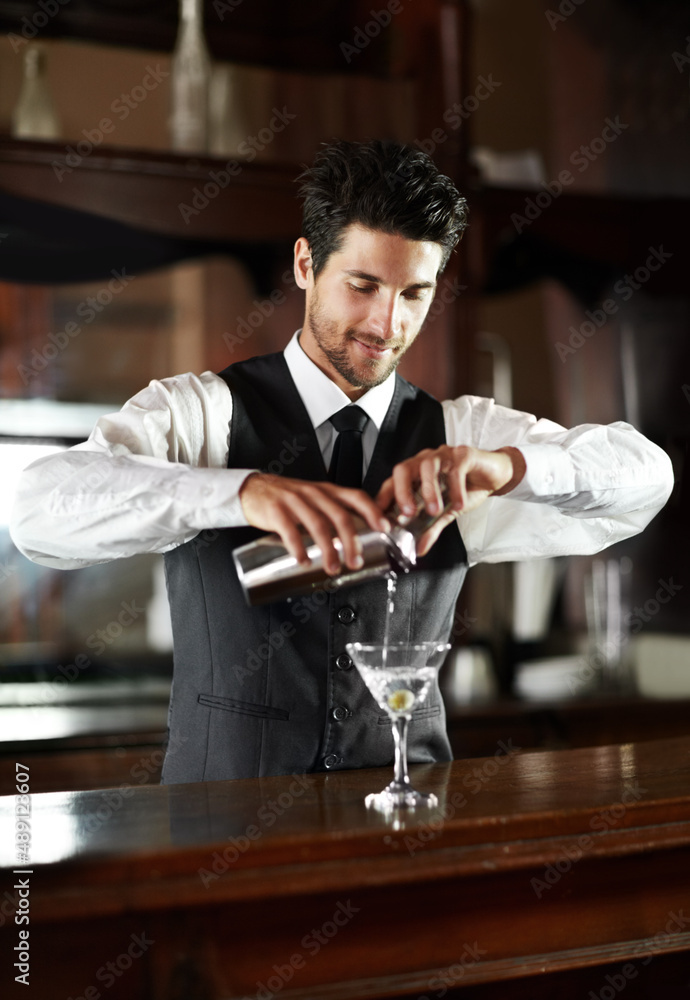 Master mixologist. A handsome young bartender mixing a cocktail for a customer.