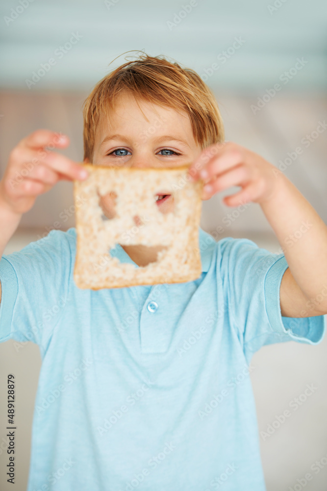 Food makes me happy. Shot of a little boy holding up a slice of bread with a cut out smiley face.