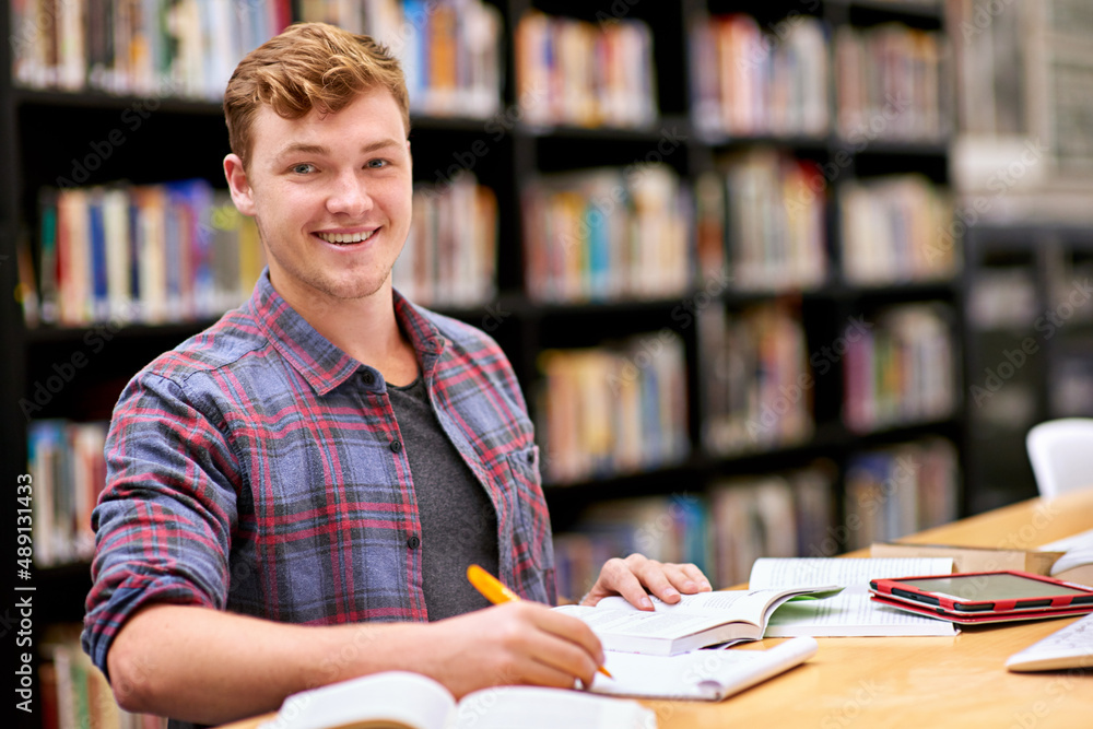 Hes top of his class. Portrait of a male student studying at a table in a university library.