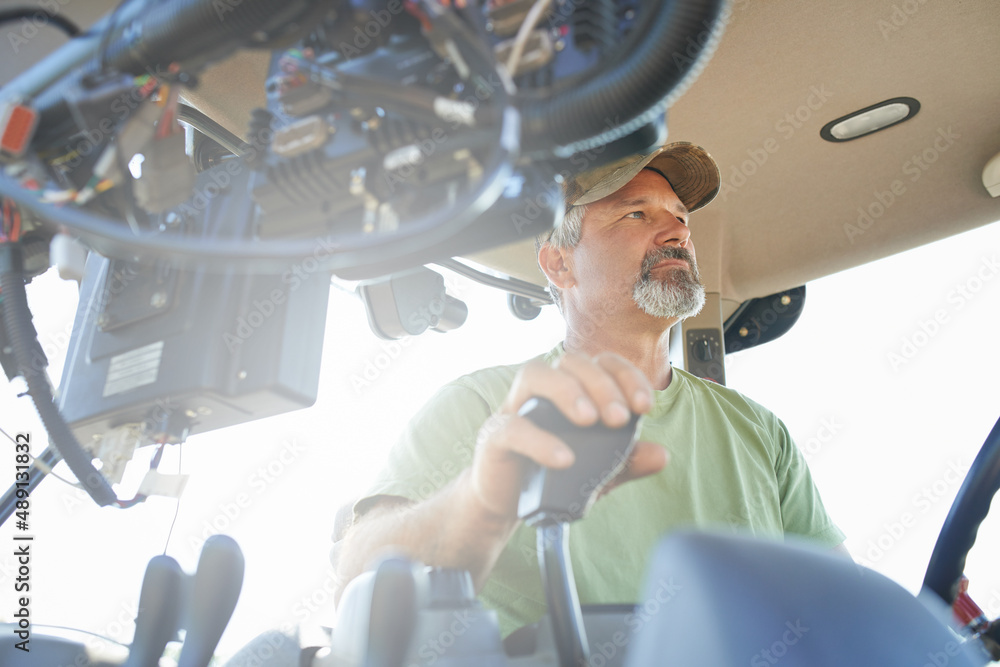 Working the fields. Shot of a farmer working inside the cab of a modern tractor.