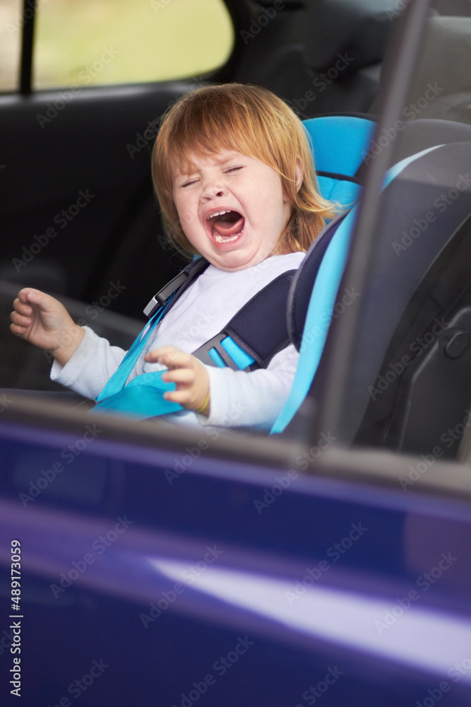 She doesnt like her carseat. A crying baby sitting in a carseat in a car.