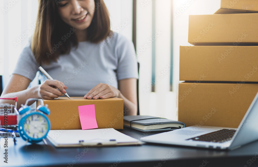 Young Asian woman running a small e-commerce start-up is working at her office desk and is writing t