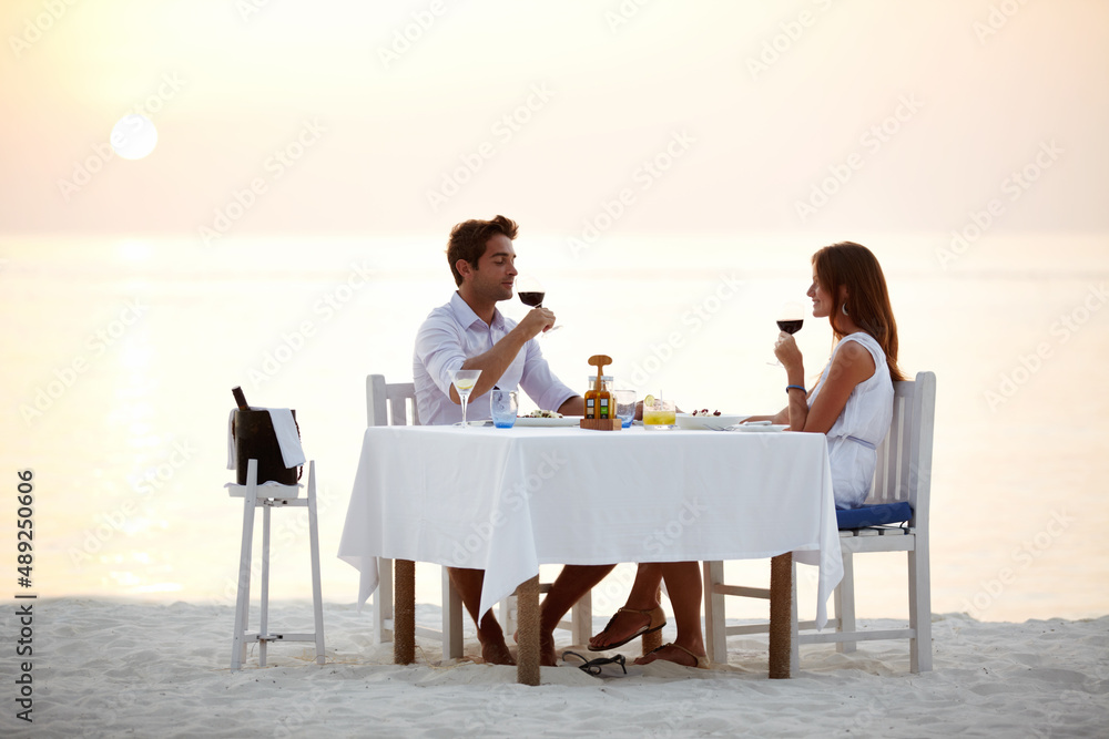 浪漫的海滩晚餐。一对年轻夫妇在海滩上吃晚餐时喝酒。