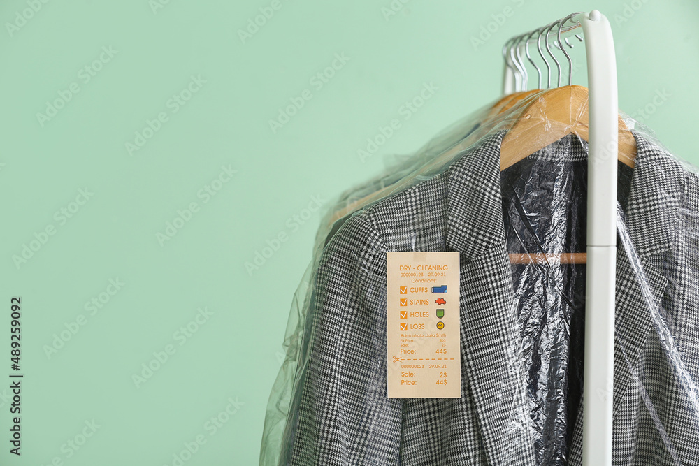 Rack with clean checkered jacket in plastic bag on green background, closeup