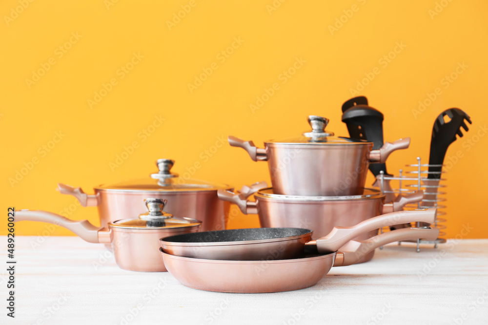 Set of copper kitchen utensils on white wooden table against orange background