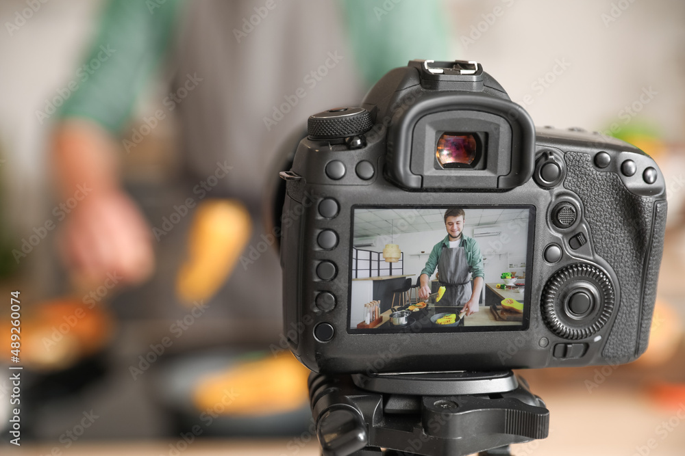 Young man cooking vegetables on display of photo camera in kitchen, closeup