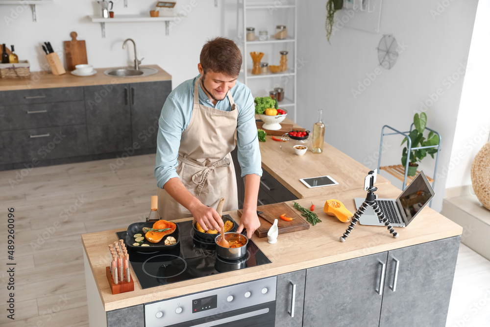 Young man cooking tasty vegetables while recording video tutorial in kitchen