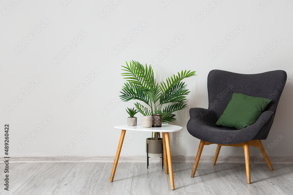 Modern armchair with table and plants near light wall