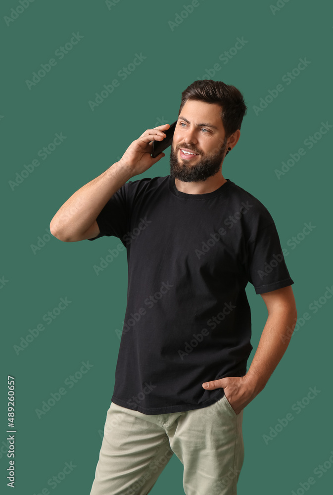 Handsome man in black t-shirt talking by mobile phone on green background