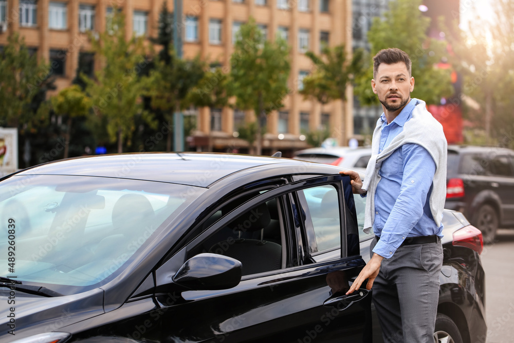 Handsome businessman closing car door on city street