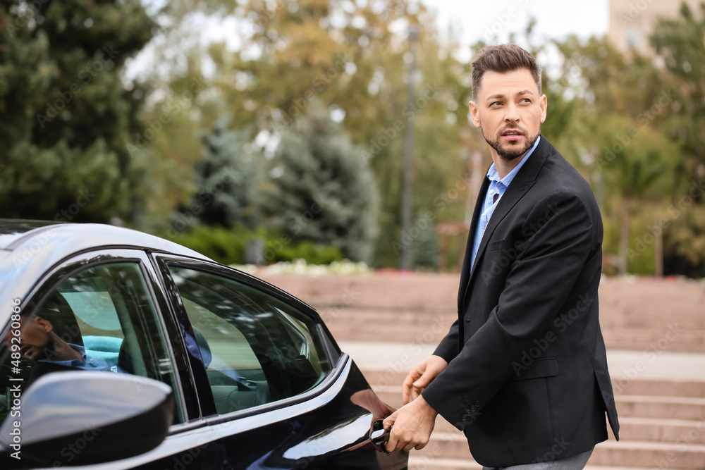 Handsome businessman opening car door on city street