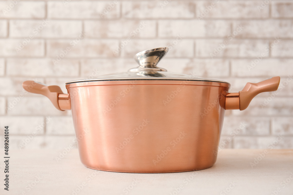 Shiny cooking pot on table against brick background