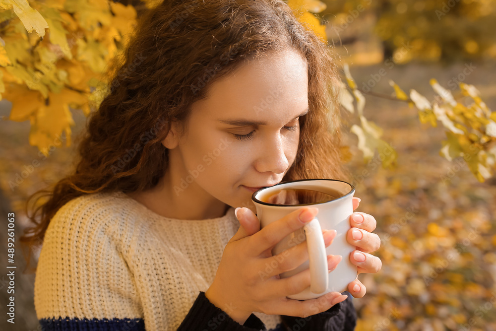 年轻女子在秋季公园喝茶