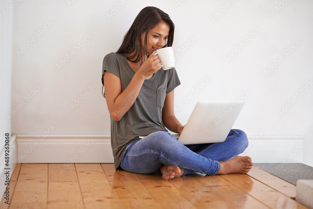 Wireless connectivit. Shot of a young woman sitting on the floor at home drinking a coffee and using