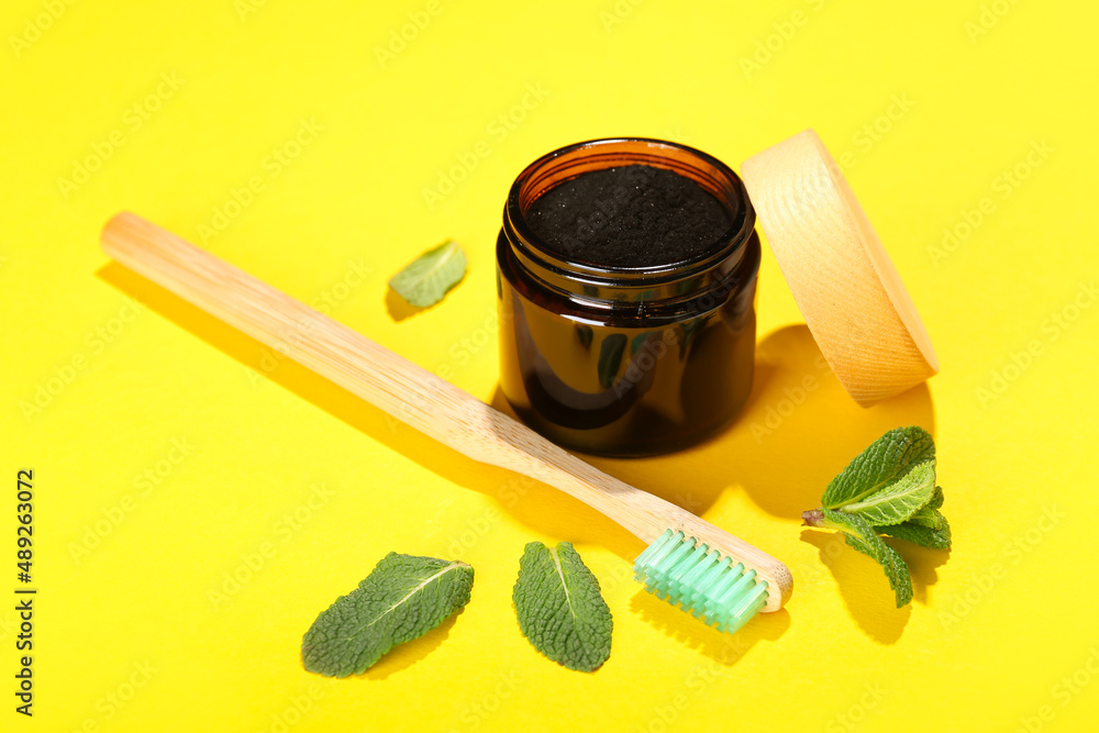 Jar with activated charcoal tooth powder and toothbrush on yellow background