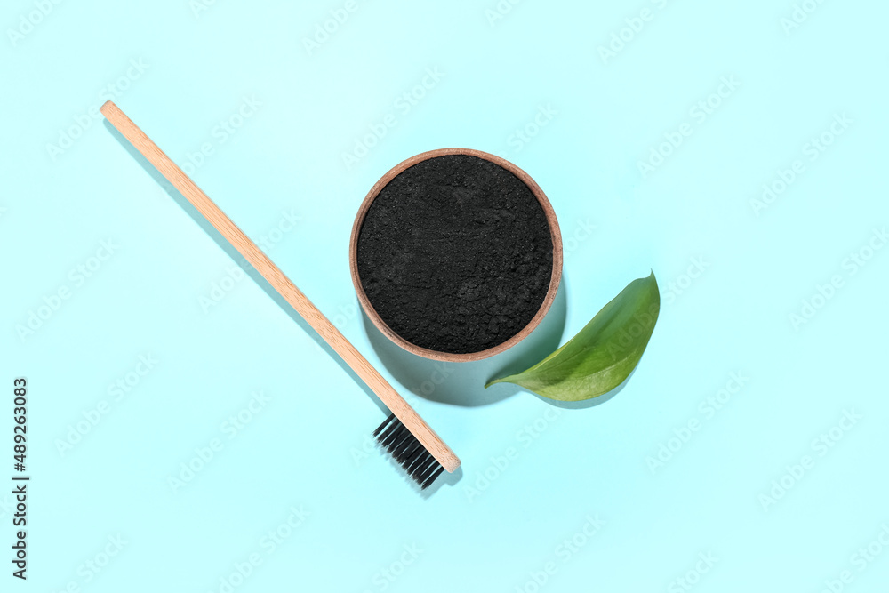 Bowl with activated charcoal tooth powder and toothbrush on blue background