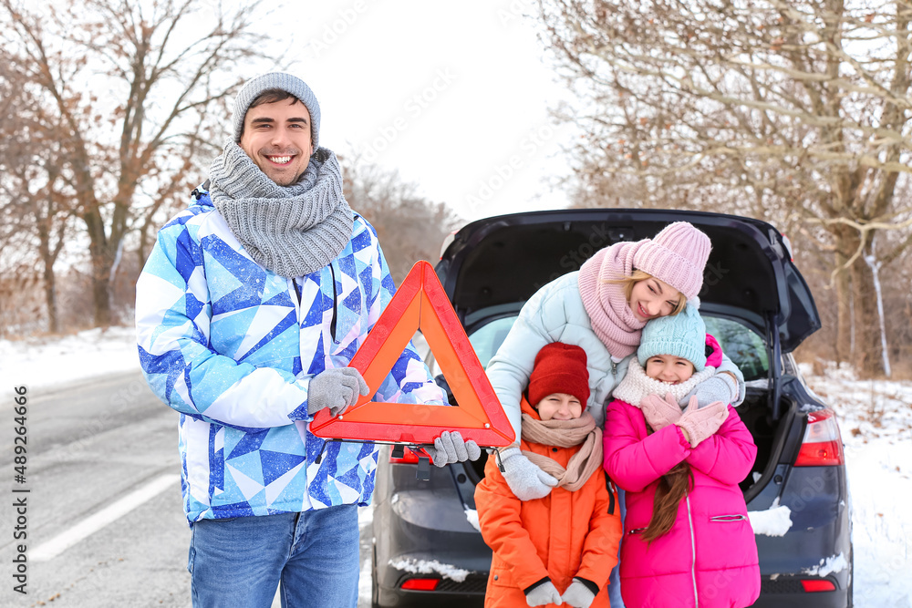 Young man with emergency stop sign and his family near broken car on snowy winter day