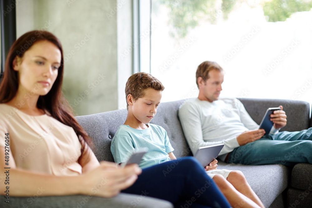 Left to their own devices.... Shot of a family of three sitting separately on a sofa with their own 